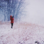 Jak przeżyć święta, by z nikim się nie pokłócić? Na zdjęciu osoba w czerwonej kurtce stoi w śniegu na wzgórzu i patrzy przez lornetkę.