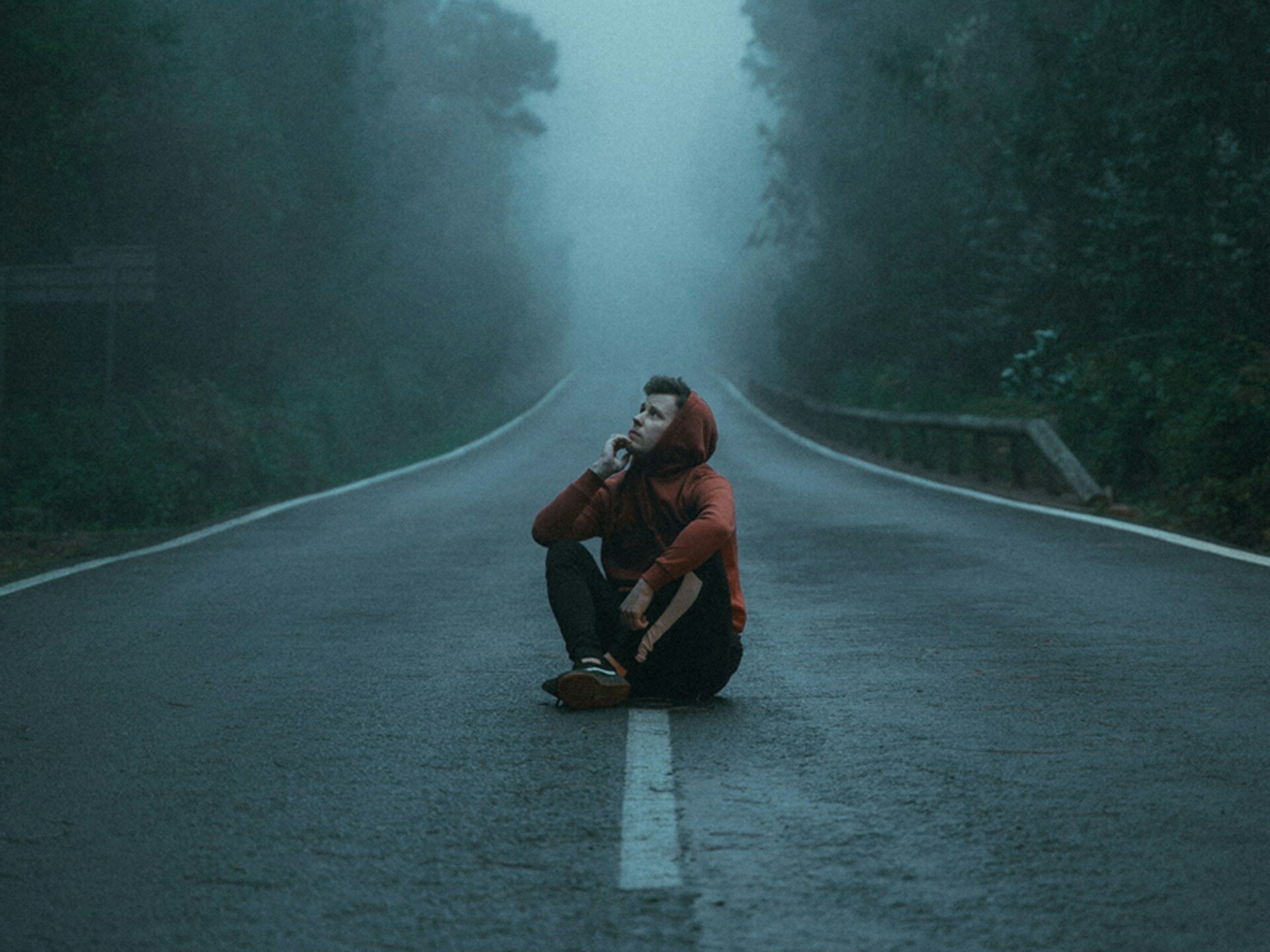 Mężczyzna w czerwonej bluzie siedzi na jezdni, mglisty dzień,