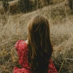 Dziewczyna w czerwonej sukience w kropki siedzi tyłem na polu, jest lato