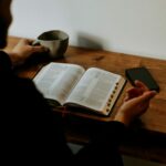 jak czytać Biblię codziennie. Na zdjęciu mężczyzna czyta Biblię przy biurku, popija kawę