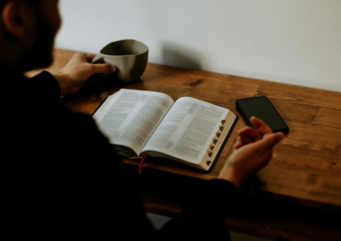 jak czytać Biblię codziennie. Na zdjęciu mężczyzna czyta Biblię przy biurku, popija kawę