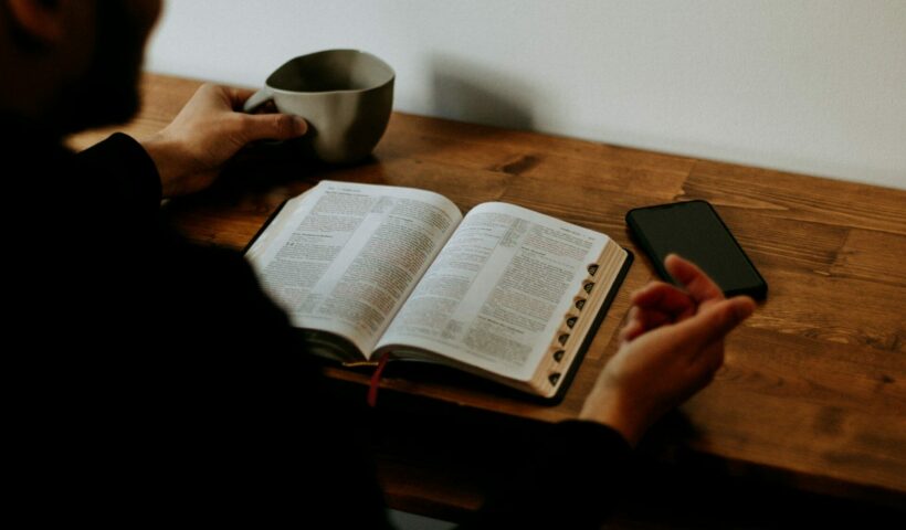 jak czytać Biblię codziennie. Na zdjęciu mężczyzna czyta Biblię przy biurku, popija kawę