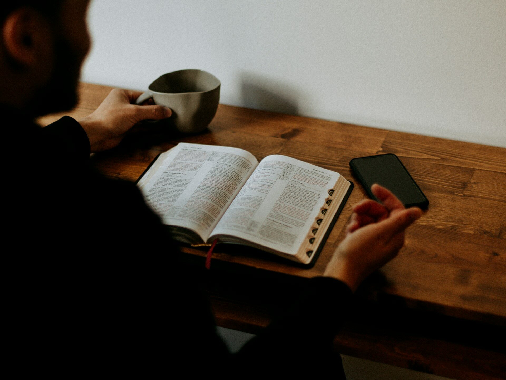 jak czytać Biblię codziennie. Na zdjęciu mężczyzna czyta Biblię przy biurku, popija kawę